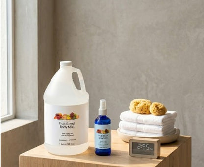 Body mist gallon, spray bottle, and towels on a wooden surface with a neutral background.