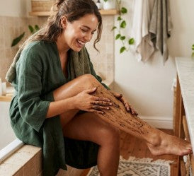 Woman sitting on a wooden stool in a bathroom, wearing a green robe.