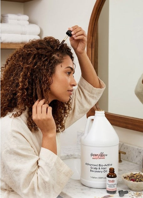 Woman applying 4everalive Labs hair scalp oil to her hair in front of a mirror with various hair care products on the counter.