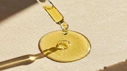 Dropper with Scalp Oil Serum with Caffeine being dripped onto a white surface